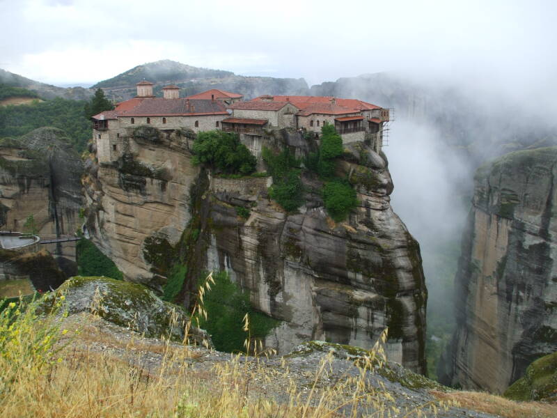 The monastery of Moni Varlaam at Meteora, on a tall rock pillar with cliff faces and clouds in the background.