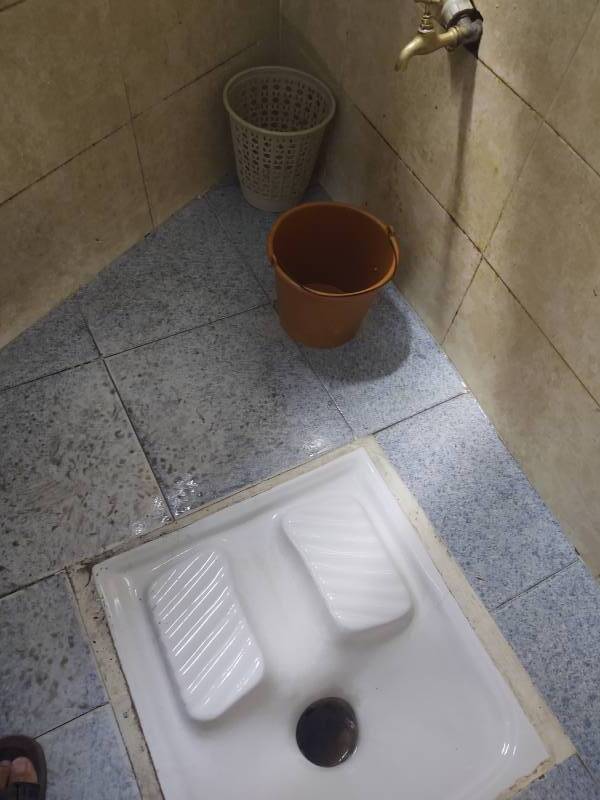 Squat toilet, water spigot, small red plastic bucket, and small green trash bin at Cafe Hafa in Tangier.