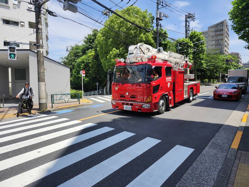 A fire truck with extending ladder system enters the intersection, preparing to turn left, to the south.