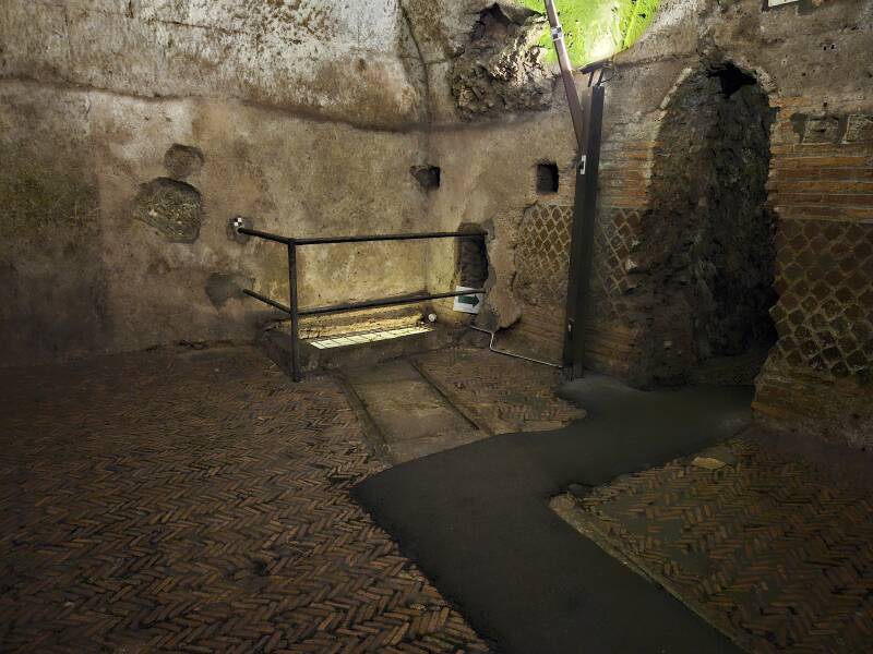 Subterranean room with a stream running beneath a grate in the corner.