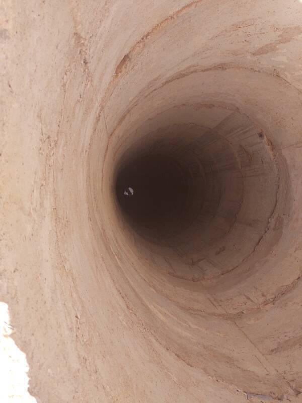 Looking down a deep government well in the Sahara desert, some water is visible at the bottom.