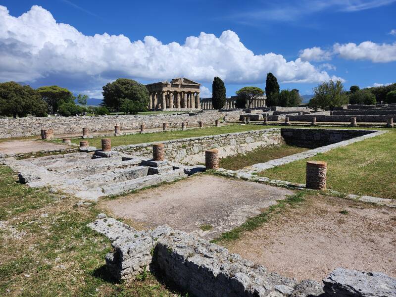Swimming pool surrounded by a columned portico with two large temples in the middle distance.