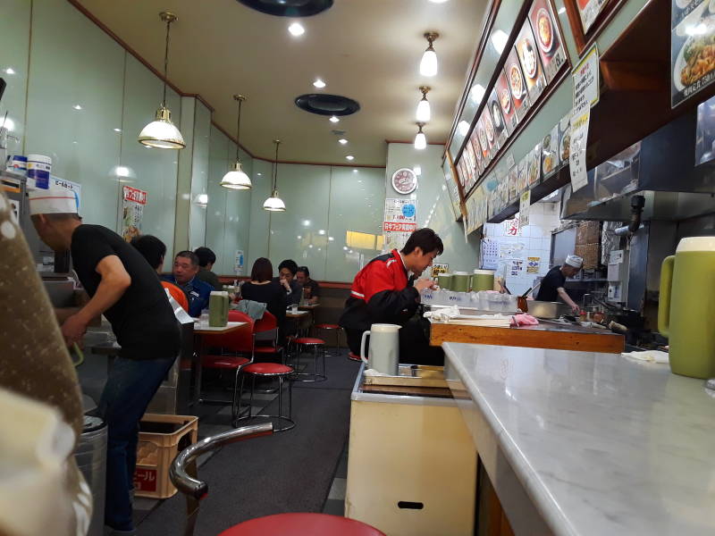 Getting lunch a noodle shop in Osaka, looking down the counter, other patrons at small tables.